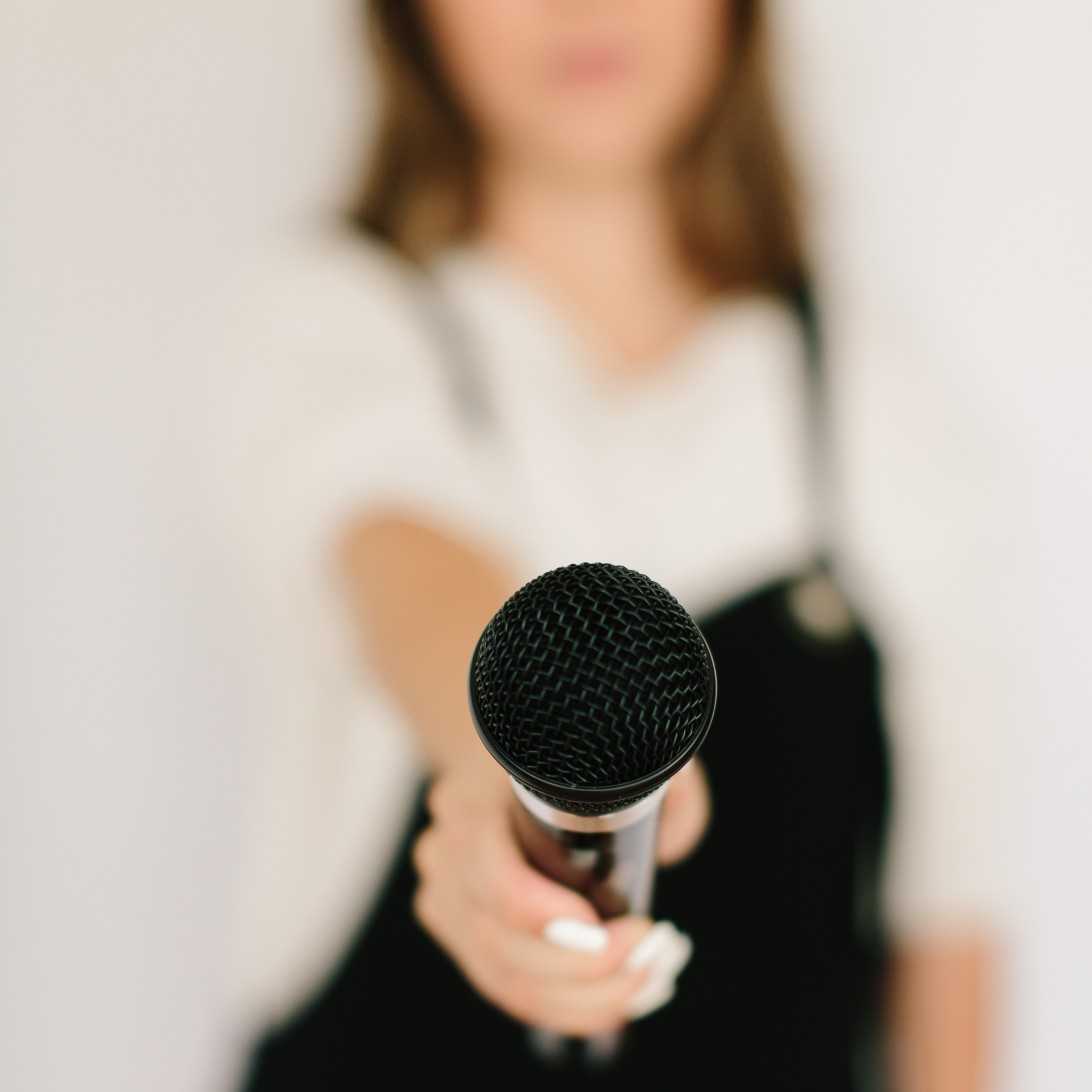 As though Mary could accept the microphone and introduce herself to you directly, an event host holds out a microphone.