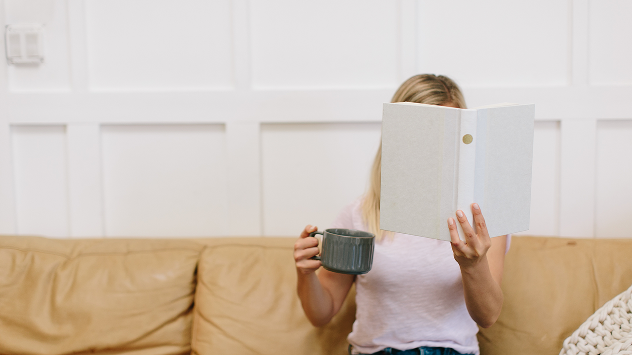 woman reading a book holding a cup of coffee